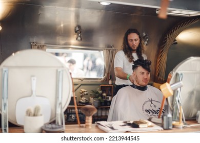 London UK - August 7, 2021:  Hairstylist Doing Haircut In Mobile Hair Salon At Classic Car Boot Sale, A Retro Culture Festival.