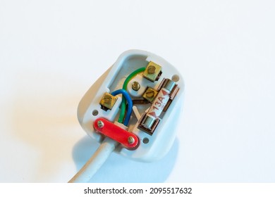 LONDON, UK - CIRCA 2021 DECEMBER: A UK 13 amp white plug against a white background. Wired with a 3 core power cable, brown live, blue neutral, and green earth. Fitted with a 13 amp fuse. Close-up.