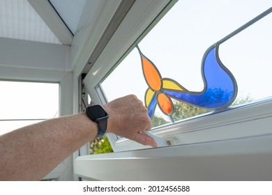 London, UK - Circa July 2021: Person Seen About To Shut An Ornate, Leaded Window Within A Residential Conservatory. The Ornate Style And Coloured Glass Of The Small Window And Latch Is Evident.