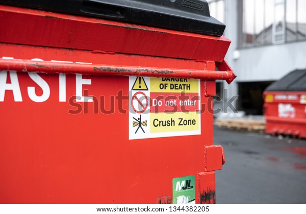 London, UK - Circa March 2019: Details view of an\
industrial waste container seen outside a printers. Various safety\
icons are seen on the red bin, as part of health and safety at\
work.
