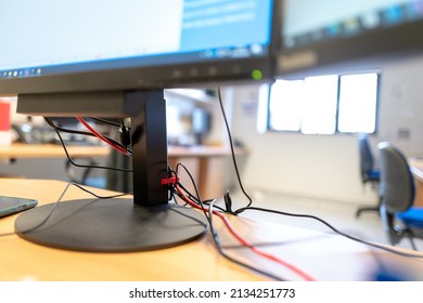 London, UK - Circa March 2022: Shallow Focus Of Messy Cables Seen At The Base Of A Large Computer Monitor. Located On A Desk And Seen In A Large Office Environment,