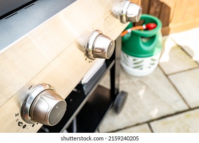 London, UK - Circa May 2022: Shallow Focus Of The Nearest Gas Control Knob Seen In A Large, Gas Powered BBQ On A Patio. A Nearby Gas Bottle Can Be Seen, Feeling The BBQ.