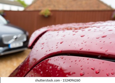 London, UK - Circa October 2019: Shallow Focus Of A Newly Washed, Red Coloured New Car Showing The Water Droplets On The Bodywork. A Parked SUV Is In The Distant, On A Private Driveway.