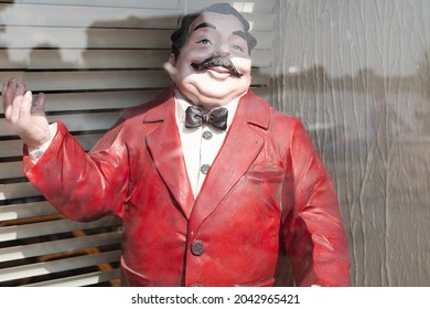 London, UK - Circa September 2021: Large plastic model of an Italian waiter seen in a restaurant window. Used to welcome guests, reflections can be seen of a nearby quay side in late summer.