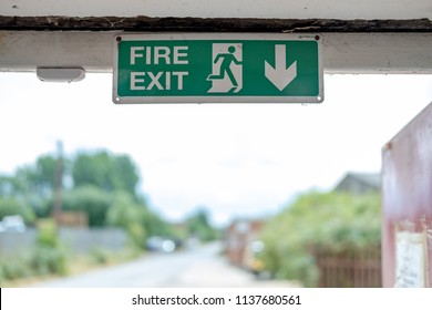 London, UK - Crica July 2018: Shallow Focus, Isolated Image Of A Green Fire Exit Sign Seen Attached An Internal Factory Door Frame, Leading To The Outside Of The Factory For Fire Emergencies.