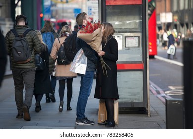 London, UK - December 22, 2017: A Loving Couple With Red Shrubbery Stands Near The Phone Booth Near Liverpool Street