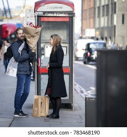 London, UK - December 22, 2017: A Loving Couple With Red Shrubbery Stands Near The Phone Booth Near Liverpool Street