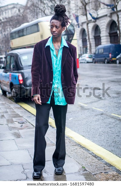 LONDON, UK-\
February 15 2020: Fashionable people on the street during Fashion\
week . Street style. Seventies style man with dreadlocks in a dark\
brown suede suit and green\
shirt.