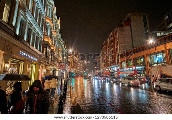 LONDON, UK - FEBRUARY 2017: Night traffic and street\
scenery in a typical rainy day in United kingdom near Harrods\
Department Store in London. Night urban scene during Winter period\
in London, UK