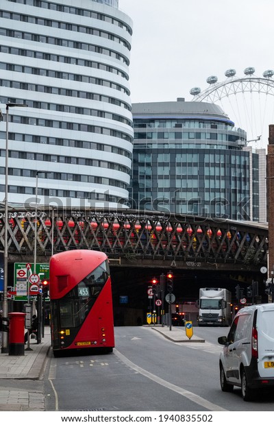 London UK February 2021 London double decker city\
bus stopped on a bus stop, streets empty with no cars during UKs\
national covid lockdown. Tube train passing over the overpass\
bridge