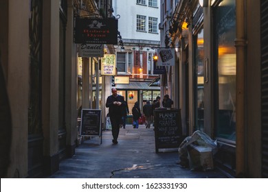 London, UK - January 19, 2020: Dark Alley In East London, Near Bank Area And The City. A Man Walks Through A Narrow Street With Pubs And Shops. Some Litter On The Street