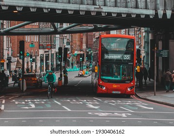 London UK January 2021 View Of A Double Decker London Bus Passing Under A Train Bridge. People Walking On The Streets During UKs Third National Covid Lockdown