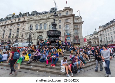 LONDON, UK - JULY 20, 2015: Tourists Sitting On The Steps Of The Shaftesbury Memorial Fountain In Piccadilly Circus In City Of Westminster. It's A Road Junction And Public Space Of London's West End.