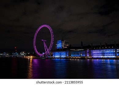 London, UK. July 20, 2021. Illuminated London Eye On The Banks Of River Thames In Front Of Lit Urban City Buildings And County Hall