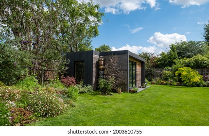 London UK. July 2020. Suburban Garden In Pinner, Middlesex. Rock Garden In The Foreground. Garden Office With Black And Cedar Cladding And Green Roof Behind.