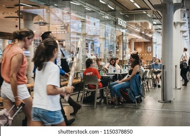 London, UK - July 26, 2018: People Sitting At Table In A Cafe Inside St. Pancras Station, People Rushing Past Them. St. Pancras Is One Of The Largest Railway Stations In London And A Home To Eurostar.