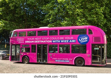 London, UK - July 5, 2022: Pink Double Decker Public Bus With Ad On Side For Wizz Air On Albany Street, Green Foliage In Back.