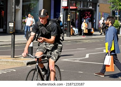 London, UK - June 2022: Person Looking Down At His Mobile Phone While Riding A Biycycle Along Oxford Street