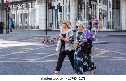 London, UK - June 21, 2022: Two women with flower are crossing the road in the City of London. Commuters, office workers, City of London life, Street photography