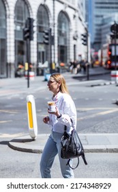 London, UK - June 21, 2022: Young woman with coffee cup walking on the City of London. Commuters, office workers, City of London life, Street photography