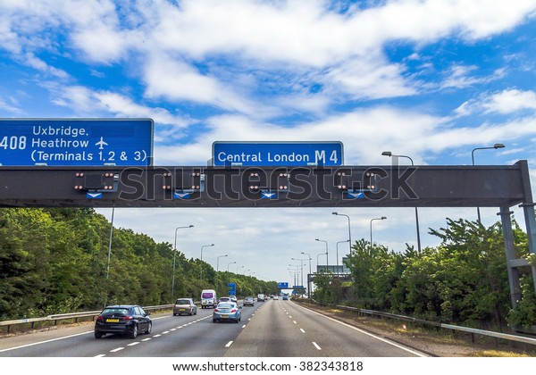 LONDON, UK - JUNE 5, 2015:\
Intensive left-hand traffic on British four lane motorway M4   with\
active electronic overhead information sign at grey cloudy  summer\
day 