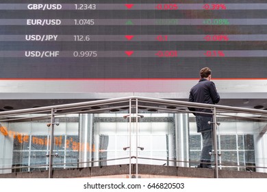 London, UK - May 15, 2017 - Stock Market Data Displayed On A Outdoor Screen In Canary Wharf With A Man Standing In Front Of It