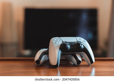London, UK - May 25, 2021: Two Playstation 5 (PS5) controllers on the table, tv on background, selective focus. Playstation 5 is the latest video game console from Sony release in November 2020.