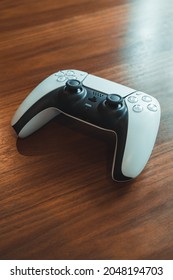 London, UK - May 25, 2021: White Playstation 5 (PS5) wireless controller on a wooden table, selective focus. Playstation 5 is the latest video game console by Sony released in November 2020.