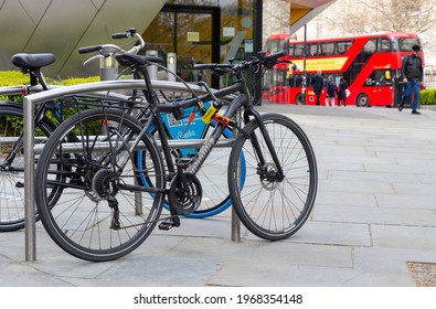 London, UK - May 5, 2021: A black bike chained in a London street with two locks. Red bus in the background