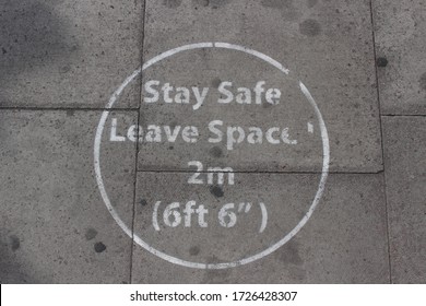 London / UK - May 8 2020: 'Stay Safe Leave 2 Metre Space' Message Spray Painted Onto A London Pavement During Covid 19 Lockdown