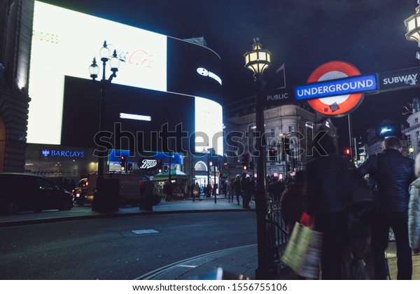 London, UK - Nov. 08, 2019: Long exposure of\
famous Piccadilly circus intersection with big neon LED advertising\
screens. London buses and crowed of people crossing by. Night time\
scene.
