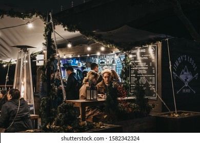 London, UK - November 24, 2019: People At A Bar Within Southbank Centre Winter Market, An Outdoor, Global Street Food Market, Focused On Sustainable And Artisan Produce. Selective Focus, Motion Blur.