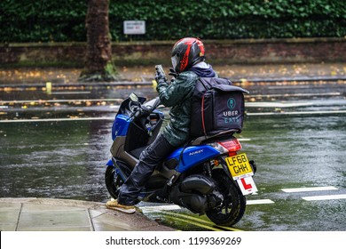 LONDON, UK - OCTOBER 06, 2018: UBER EAT, Food Delivery  Motor Bike Driver Checking The Addresses Under Rain.