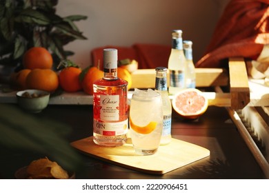 LONDON, UK - OCTOBER 10, 2022: Gin Tonic Cocktail Glass With Pomelo Peel, Bottle Of William Chase Pink Grapefruit And Pomelo Gin And Sicilian Lemonade Fever Tree Tonic In The Background.