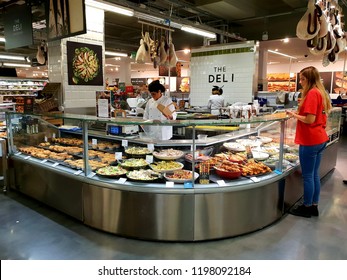 London, UK, October 8th 2018: A Shop Worker Behind The Deli Counter Preparing Assortment Of Fresh Meat And Vegetables, Whilst A Customer Looks On