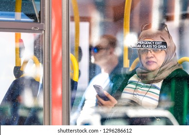 London, UK - September 13, 2018: Muslim Arab Woman In Headscarf Hijab Portrait Closeup Sitting On Bus Transportation In City With Emergency Exit Sign Through Window