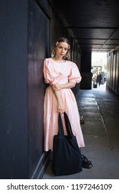 LONDON, UK- SEPTEMBER 14 2018: People On The Street During The London Fashion Week. The Blonde Girl In A Pink Dress In The Sixties Style Stands By The Black Wall