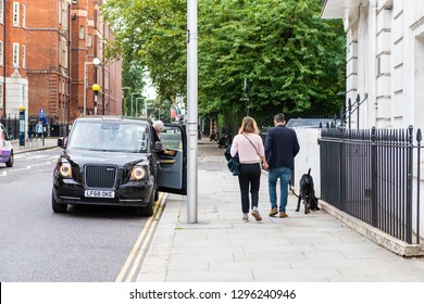 London, UK - September 16, 2018: Neighborhood District Of Chelsea And Brompton In Kensington With Couple Walking On Sidewalk Pavement With Dog And Black Taxi Cab