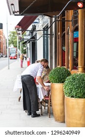 London, UK - September 16, 2018: Man Waiter Standing Setting Up Cafe Dining Table In Chelsea Outside Restaurant Street Sidewalk During Day