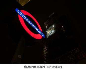 LONDON, UNITED KINGDOM - 15. April 2019: Illuminated Underground Sign In Front Of The Big Ben Clock. Public Transport Symbol At Night In The City. Subway Entrance In Westminster.