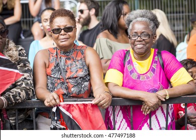 London, United Kingdom - August 29, 2016:  Notting Hill Carnival. Two Older Women Stand On A Barrier To Watch The Parade Go By And To Remember 40 Years Ago When They Were The Ones Dancing By.