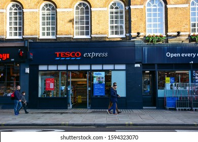London / United Kingdom — December 15, 2019: people walk by the front of Tesco Express store on the street in London. Tesco is one the largest UK supermarket chains. It sells food and groceries
