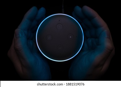 London, United Kingdom - December 19 2020: Hands around an illuminated Amazon Echo Dot smart speaker with built-in Alexa voice assistant.