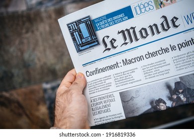 London, United Kingdom - FEb 2, 2021: POV Male Hand Holding Reading French Le Monde Newspaper With Lockdown Confinement And Macron Seeking Solutions Headlines