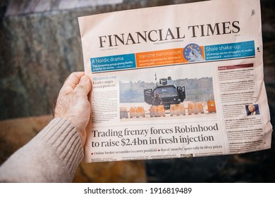 London, United Kingdom - FEb 2, 2021: POV Male Hand Holding Financial Times Newspaper Reading About The Myanmar Coup And The Trading Frenzy About Robinhood App