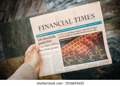 London, United Kingdom - FEb 2, 2021: POV Male Hand Holding Financial Times Newspaper Reading About The Reddit Stock Rally And Anti Covid Vaccine Crisis