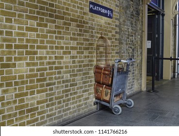 London, United Kingdom, June 2018. Platform 9 and 3/4 at Kings Cross Station, London. A trolly stuck in the wall where fans emulate the Harry Potter adventures. A service assistant for the photo.
