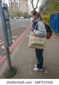 London, United Kingdom - March 30, 2020: Unknown Young Woman Wearing Virus Mouth Face Mask Checking The Bus Timetable. Increasingly People Wear Masks During Coronavirus Covid-19 Outbreak In UK