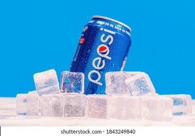 London, United Kingdom - October 29 2020:  Ice cold can of Pepsi sits on a pile of frozen ice cubes with condensation on a marble surface against a blue wall.