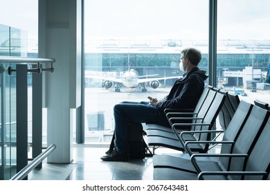 LONDON, UNITED KINGDOM - Sep 29, 2021: A Male With A Protective Mask Sitting Alone At The Airport With An Airplane Behind In London, UK